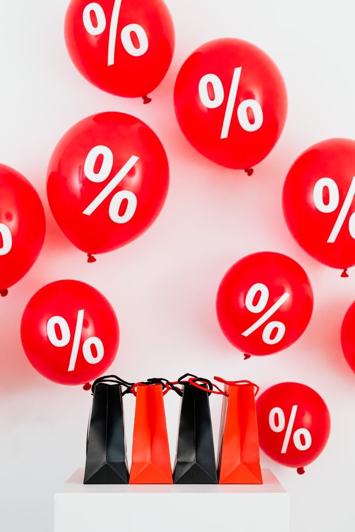 Red and black shopping bags on a white background with red balloons featuring percentage symbols, ideal for sales.