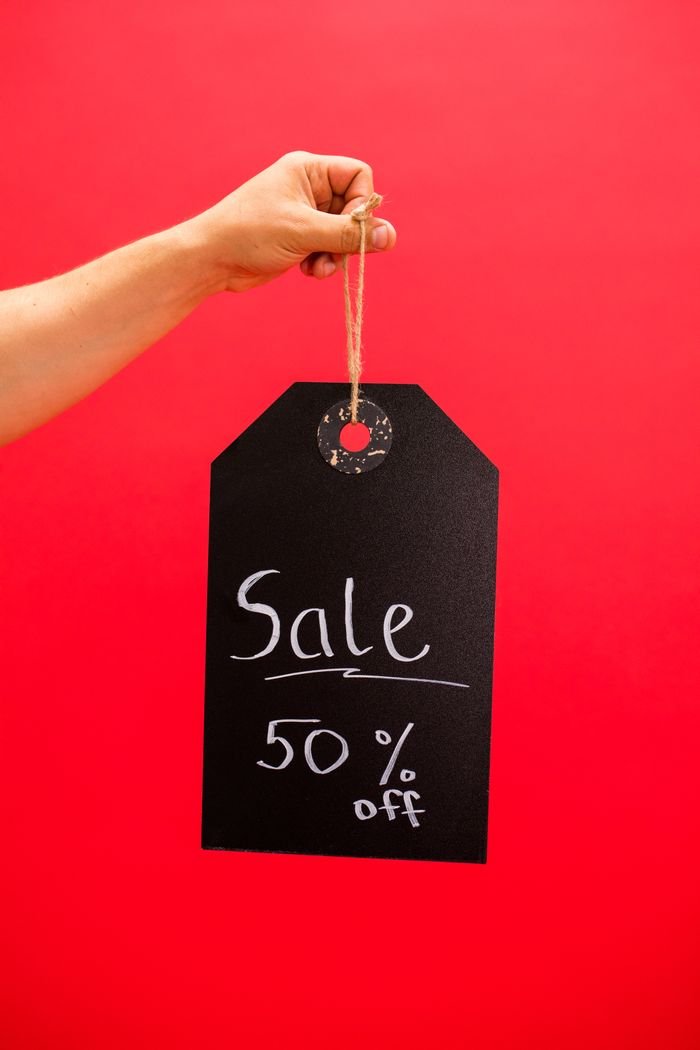 Hand holding a black sale tag with 50% off on a red background.